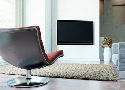 Support TV mural Vogel's THIN RC355 noir, fauteuil rouge moderne, tapis beige, mur blanc, écran TV noir, vase blanc