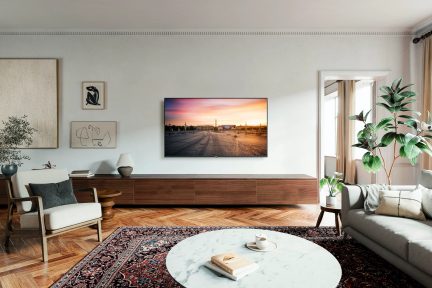 Moderní obývací pokoj s dřevěnou podlahou, perským kobercem, kulatým mramorovým konferenčním stolkem, šedou pohovkou, křeslem, dřevěným televizním nábytkem, televizí na stěně, 3 obrazy a zelenou rostlinou.