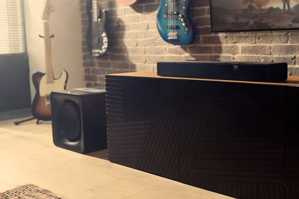 Černý soundbar Klipsch se subwooferem, umístěný na designové dřevěné skříňce v hudebním obývacím pokoji s cihlovou zdí