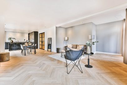 Moderní obývací pokoj s světlými parkety, šedou pohovkou, modrými křesly, černým konferenčním stolkem, velkými francouzskými okny a vestavěnými bodovými světly ve světlém stropu.
