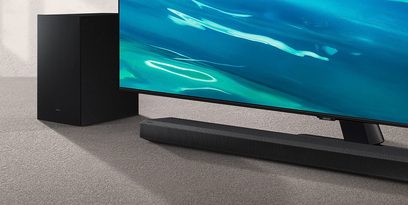 Samsung HW-Q700A/ZF soundbar og subwoofer, sort, foran et TV-apparat der viser et abstrakt blåt og grønt billede