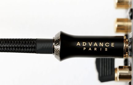 Sort, satinmetal audioforbinder med gylden "ADVANCE PARIS"-påskrift, mørk rillet ring, kabel med sort flettet nylonkappe, sidebillede i ultranær af den gyldne base i baggrunden