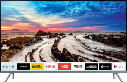 „Samsung" UE75MU7005 televizorius, rodantis uolėtą pakrantės peizažą saulėlydžio metu, matomas iš priekio ant sidabrinės kojelės, su integruota garso sistema ir nuotolinio valdymo pultais
