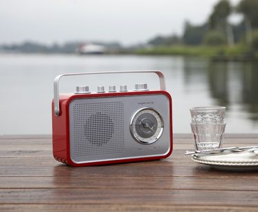 Rød og sølv bærbar Tangent Uno 2Go-radio, set forfra, stående på et træbord ved siden af et glas vand
