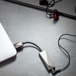 To sølvfarvede bærbare Astell&Kern PEE51 lydkonvertere forbundet med sorte flettede kabler på en grå tekstureret overflade