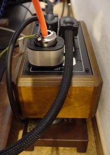 Nærbillede ovenfra af Furutech NCF Booster Brace Single i træ, med sort flettet kabel tilsluttet stikket