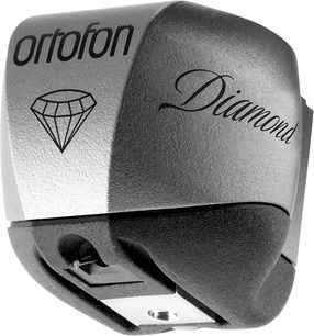 Cápsula de tocadiscos Ortofon MC DIAMOND, vista en primer plano, ángulo de vista ligeramente de lado, parte frontal visible, cuerpo gris metalizado, logotipo de diamante e inscripción "Diamond" en negro, aguja de lectura en la parte inferior