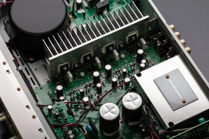 Iekšējais skats uz Marantz PM6007 sudraba zelta hi-fi pastiprinātāju, kurā redzami elektroniskie komponenti uz zaļas drukātās shēmas plates