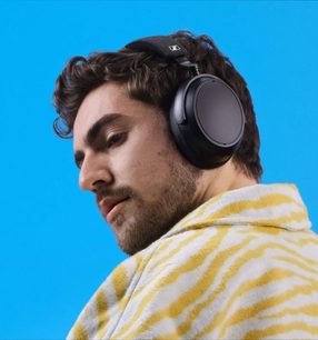 Sennheiser Momentum 4 Wireless sort omkringliggende hovedtelefoner båret af en mand i profil på en ensfarvet blå baggrund