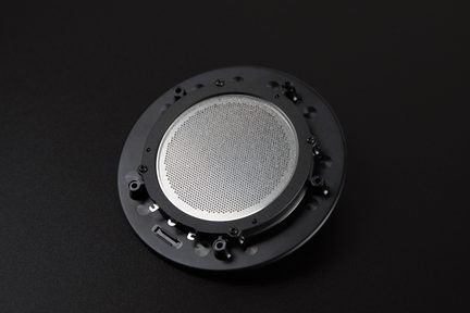 Black circular speaker with silver metal grille, top view, black background