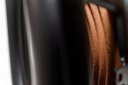 Close-up van een glanzend zwarte subwoofer met membraandetail en kopervlechtwerk