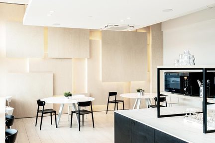 Moderner Cafeteria-Bereich mit runden weißen Tischen und schwarzen Stühlen, heller Holzvertäfelung und Marmortheke mit Mikrowelle