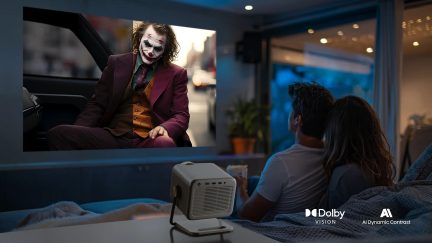 Videoprojetor branco num suporte, com projeção do Joker numa parede em frente a um casal sentado