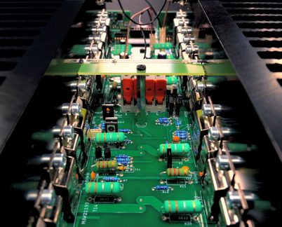 Close-up view of a printed circuit board with green resistors, capacitors, transistors, and metallic components