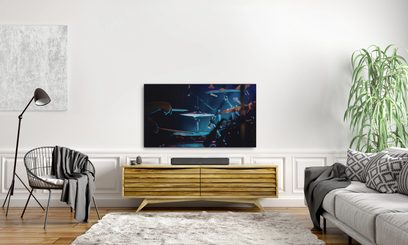 Black Denon Home 550 soundbar under a TV in a modern living room, front view