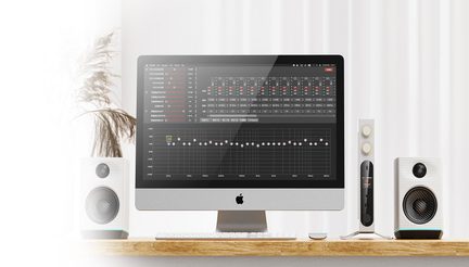 Postazione di lavoro minimalista vista frontale, composta da un computer all-in-one in alluminio grigio argento con ampio schermo nero, affiancato da due diffusori compatti bianchi con finitura scanalata e da un controller audio verticale bianco con manopole dorate, il tutto posizionato su una mensola in legno chiaro