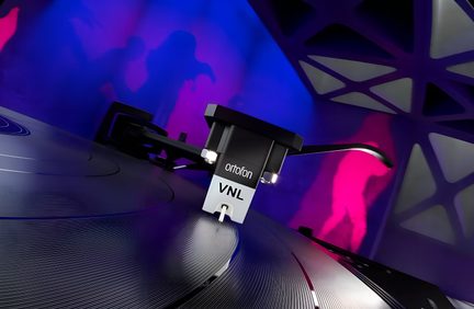 Close-up oblíquo de uma célula fonográfica Ortofon VNL preta e cinza em plástico e metal sobre um disco de vinil