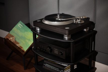 Giradischi nero posato su un mobile in legno, visto di fronte e di tre quarti, con dischi in vinile accanto