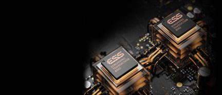 Vista macro obliqua di due chip elettronici quadrati in plastica nera opaca, con logo in rame visibile, montati su substrati traslucidi e collegati alla scheda madre nera tramite fasci di fili dorati