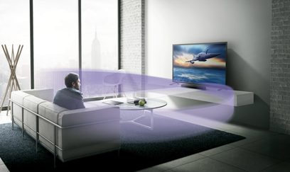 Yamaha SR-C20A sort soundbar i sort under et fjernsyn, der viser et fly i en moderne stue med en mand, der sidder på en sofa