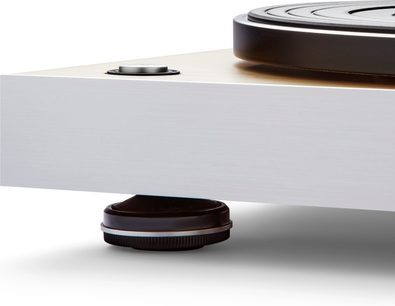 Primo piano dell'angolo anteriore sinistro del giradischi hi-fi Roberts Stylus Luxe, base rettangolare in alluminio spazzolato argento con piano superiore in legno chiaro, pulsante metallico a filo sul piatto e piede cilindrico nero con texture sotto la base, prospettiva leggermente bassa