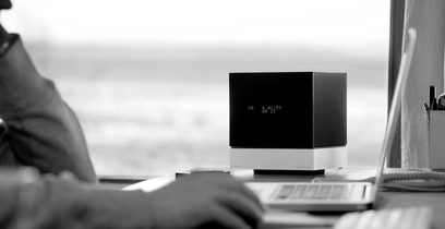 Sort Tangent Fjord Dock multimediehøjttaler, set forfra, hvid LED-skærm "CD 5 01:53 00 25", på skrivebord med bærbar computer og en persons hænder på tastaturet