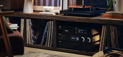 Juoda Cyrus hi-fi sistema su patefonu ir oranžine plokštele ant medinio baldo su vinilinių plokštelių kolekcija