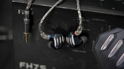 Nærbillede af to mørkeblå, kablede in-ear-hovedtelefoner i metal med røde og blå ringe samt sølvfarvede gitre på facetterede huse, forbundet med et sølvfarvet flettet kabel, set forfra