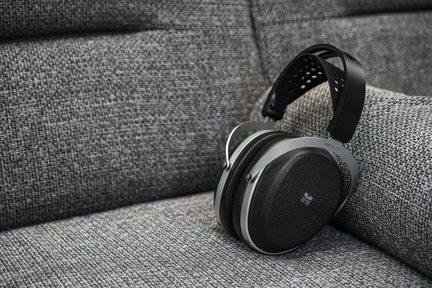 Hovedtelefoner i sort og grå metal og kunstlæder, perforeret hovedbøjle, ovale ørepuder, på grå stofsofa