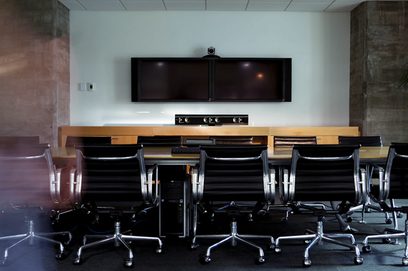 Sala conferenze con tavoli e sedie nere allineati di fronte a due schermi piatti su un mobile in legno chiaro