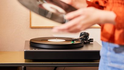 Cambridge Audio Alva ST hõbedane vinüülmängija, lähivaatest ülalt, lugemisnõel asetatud plaadile, inimese käed vinüüli käsitsemas