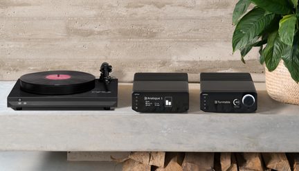 Čierna hi-fi zostava, gramofón s vinylovou platňou a prepínačom 33/45, moduly s displejom a otočným ovládačom, čelný pohľad na betónovom pozadí
