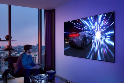 Zwarte flatscreen-tv met ultradunne metalen rand, driekwart aan de muur gemonteerd, toont een heldere scène van een raceauto met veelkleurige lichtsporen