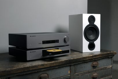 Cambridge Audio CXA61 stereoforstærker i antracitgrå og hvide bogreolhøjttalere, set forfra på et træbord