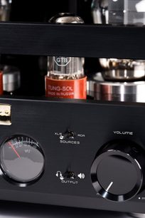 Primo piano della parte frontale in alluminio spazzolato nero del preamplificatore per cuffie Cayin HA-300MK2 argento, con grande manopola del volume circolare, vu-meter rotondo, due interruttori a levetta e valvole elettroniche visibili sullo sfondo, vista frontale