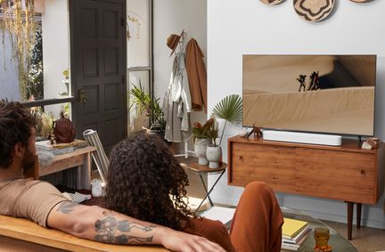 Lyst stue, skrå udsigt, tv-møbel i træ med fladskærm og hvid soundbar, potteplanter, to personer set bagfra