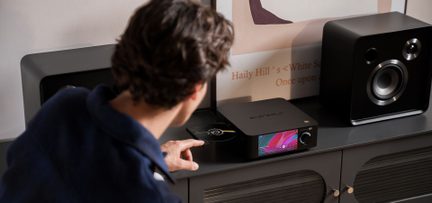 Player CD hi-fi Eversolo negru cu ecran color, între două boxe negre, vedere din trei sferturi