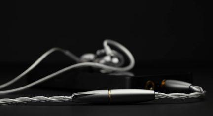 Verkabelte In-Ear-Kopfhörer mit versilbertem, geflochtenem Kabel, gebürstetem Metallstecker, unscharzer schwarzer Audio-Player im Hintergrund