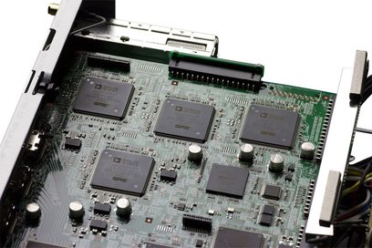 Elektronisk printkort med flere firkantede sorte mikrochips, stik og komponenter monteret på et grønt printkort