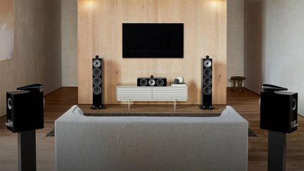 Conjunto de home cinema com colunas pretas, torres, central e de prateleira em torno de um televisor de parede