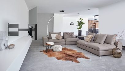 Moderne stue med grå hjørnesofa, kohudsløber, grønne planter, hvide og lysegrå lavtsiddende møbler
