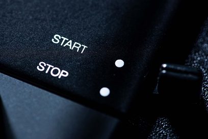 Knapper med "START" og "STOP" på en sort, tekstureret overflade, sandsynligvis af plastik eller metal, med to hvide prikker