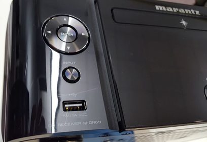Forside af en sort Marantz M-CR611-forstærker med kontrolknapper, hovedtelefonstik og display, tæt på visning