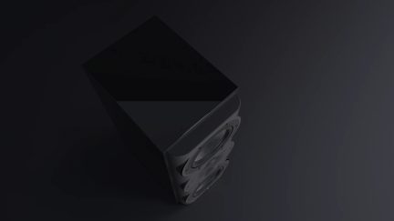 Enceinte noire vue en plongée, surface supérieure lisse, trois haut-parleurs circulaires visibles sur la face avant