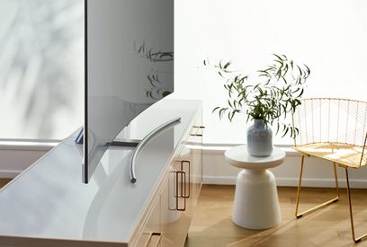 Hvid kurvet TV på metalfod i et moderne interiør med grøn plante og gul stol
