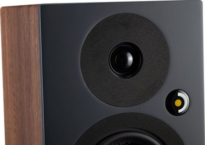Davis Acoustics Krypton 3 klasikinė riešutmedžio lentyninė kolonėlė, dalinis kampinis vaizdas, juodos matinės spalvos priekinis skydelis su centriniu aukštų dažnių garsiakalbiu, geltonas apvalus fazoinvertorius ir matomas žemų dažnių garsiakalbis.