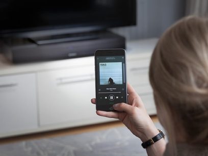 Smartphone, der viser lydafspilningsskærmen, holdt i en kvindes hånd over et hvidt computertastatur