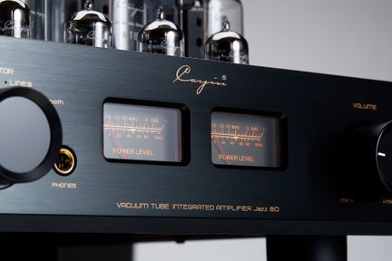 Zesilovač s elektronkami v černém kartáčovaném kovovém provedení, detailní pohled zepředu, se dvěma retro osvětlenými VU-měry v oranžové barvě, otočným knoflíkem, sluchátkovým výstupem a viditelnými skleněnými elektronkami v pozadí