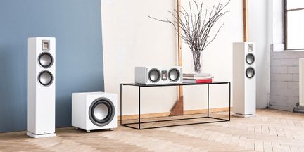 Lydsæt bestående af to gulvhøjttalere, en centerhøjttaler og en subwoofer, rektangulære kabinetter i hvidlakeret træ med grå, cirkulære højttalerenheder og rektangulære bånddiskanter, set forfra