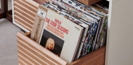 Nærbilde av en skuff i tre som inneholder vinylplater stående vertikalt, med et plateomslag synlig i forgrunnen